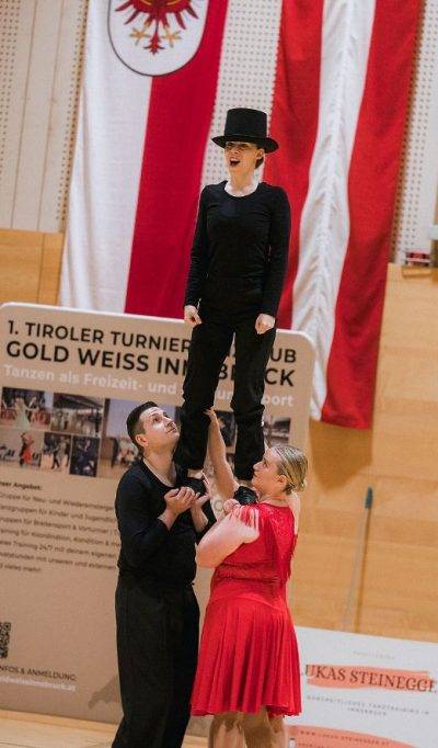 Eine Tanzgruppe in roten und schwarzen Kostümen führt eine dynamische Choreografie in einer Sporthalle auf.