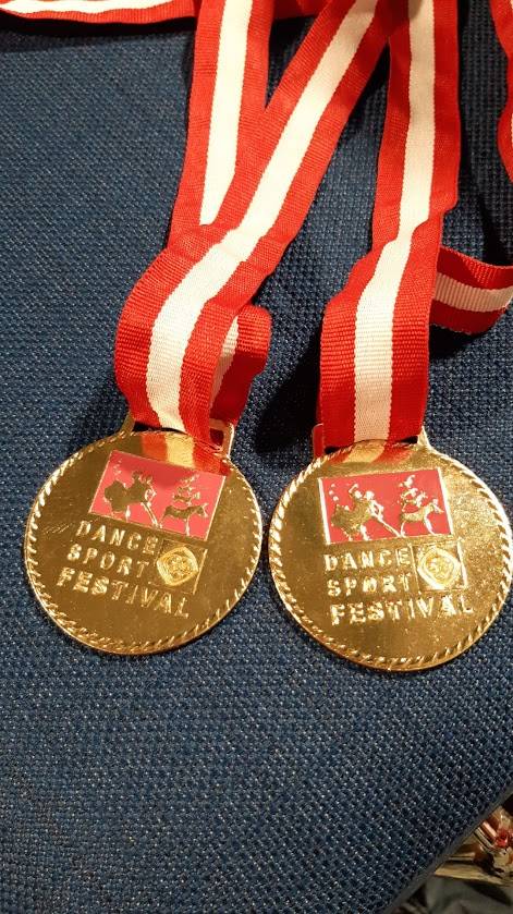 Zwei goldene Medaillen mit roten und weißen Bändern, die vom Dance Sport Festival stammen.