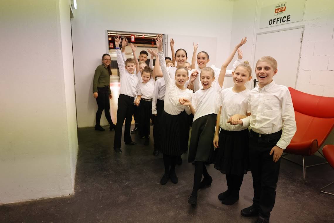 Eine Gruppe von Kindern in festlicher Kleidung posiert fröhlich vor einem Büroeingang.