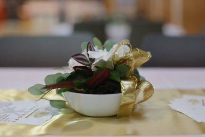 Eine dekorative Blumenarrangement in einer weißen Schale mit goldenen Akzenten auf einem Tisch.