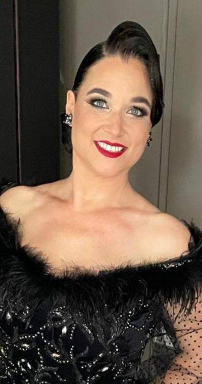 Eine lächelnde Person in eleganter, schwarzer Abendkleidung mit auffälligem Make-up.