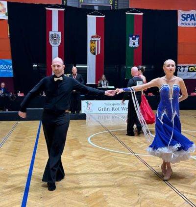 Ein Tanzpaar in festlicher Kleidung führt eine elegante Tanzroutine in einer Wettkampfumgebung vor.