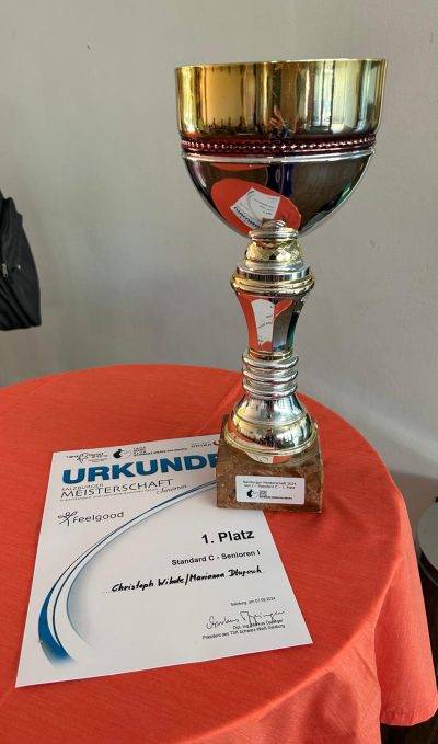 Ein Pokal und eine Urkunde, die für den ersten Platz in der Salzburger Meisterschaft 2024 in der Kategorie Standard C für Senioren ausgezeichnet wurden.